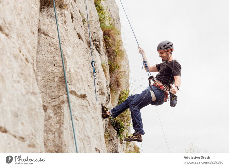 Strong male alpinist in safety equipment climbing on rocky cliff on sunny day man mountaineer rope slope strong sportswear adventure extreme athlete climber
