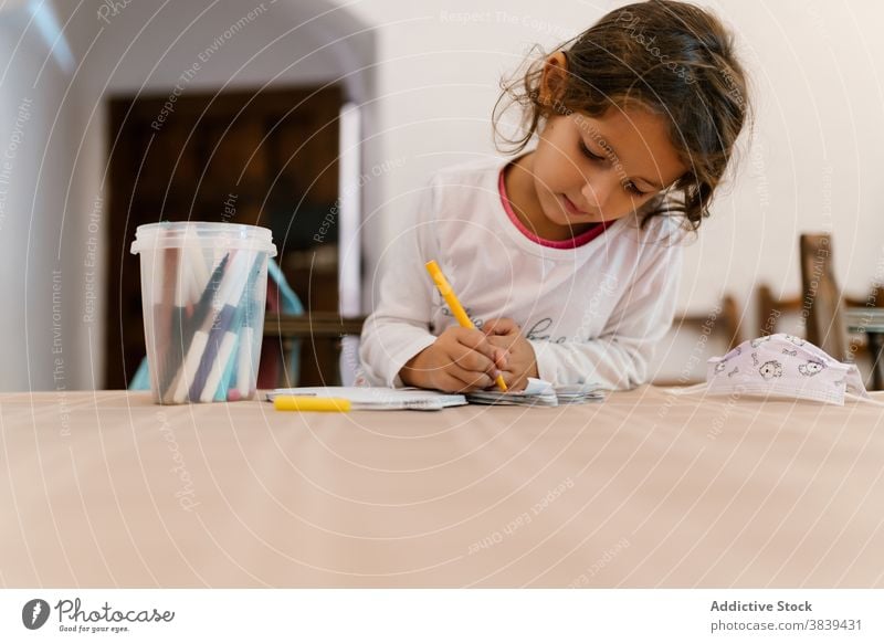 Cute girl drawing on paper at home child development kid quarantine coronavirus smart learn entertain table wooden concentrate focus mask sit creative education