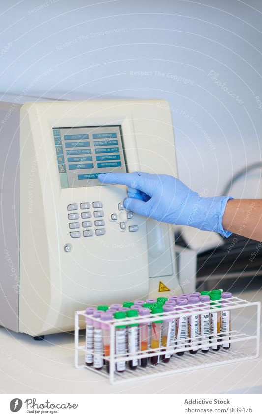 Crop scientist using blood analyzer near tubes in laboratory display analysis equipment medical modern professional device glove sterile monitor choose button
