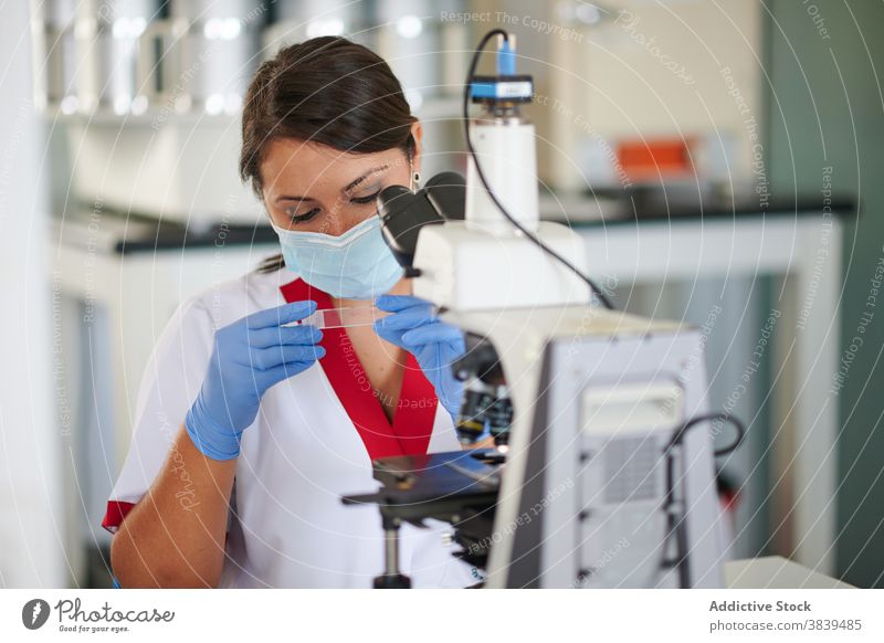 Scientist with glass sample near microscope in lab specialist medical uniform sterile profession device woman scientist professional metal material clinic work