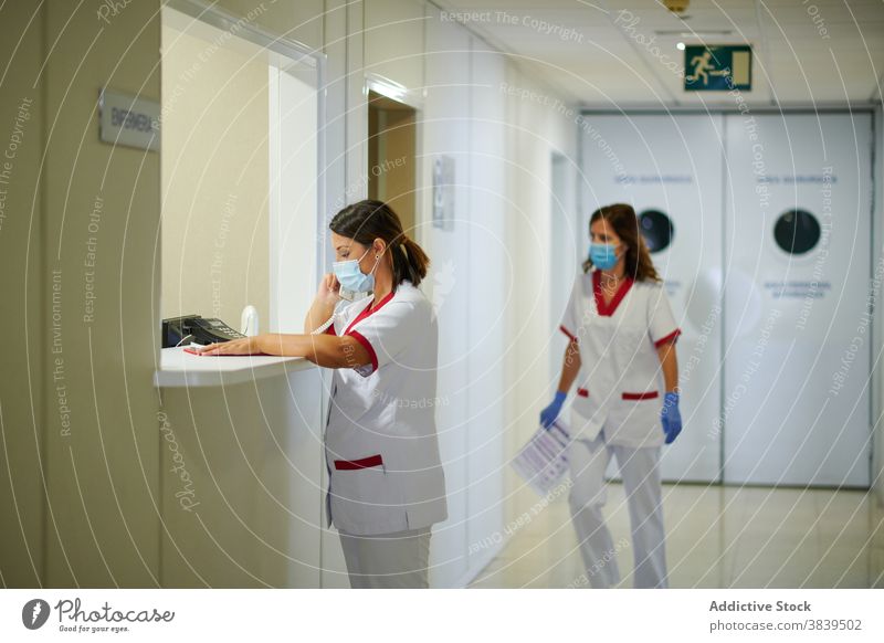 Anonymous nurse speaking on phone near colleague in clinic uniform partner medical professional corridor using device walk women phone call staff paper passage