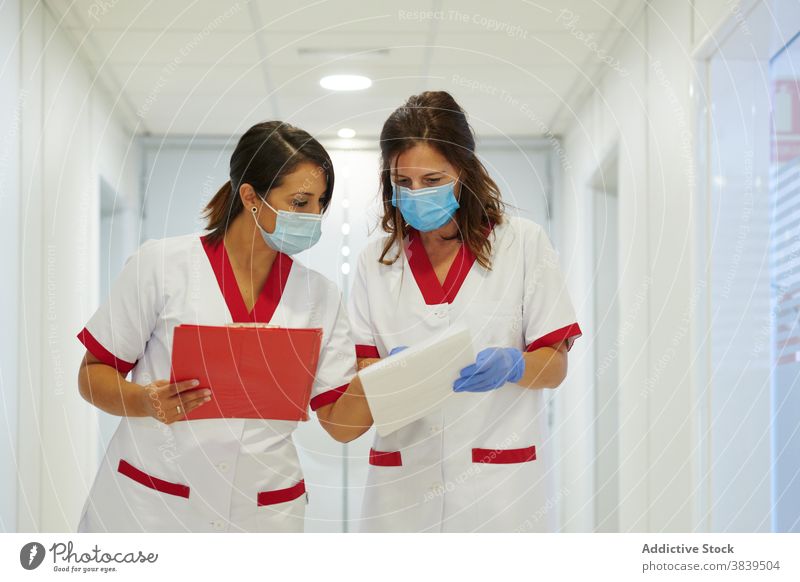 Anonymous nurses in uniforms with papers interacting in hospital passage medical staff profession walk women colleague folder colorful corridor professional