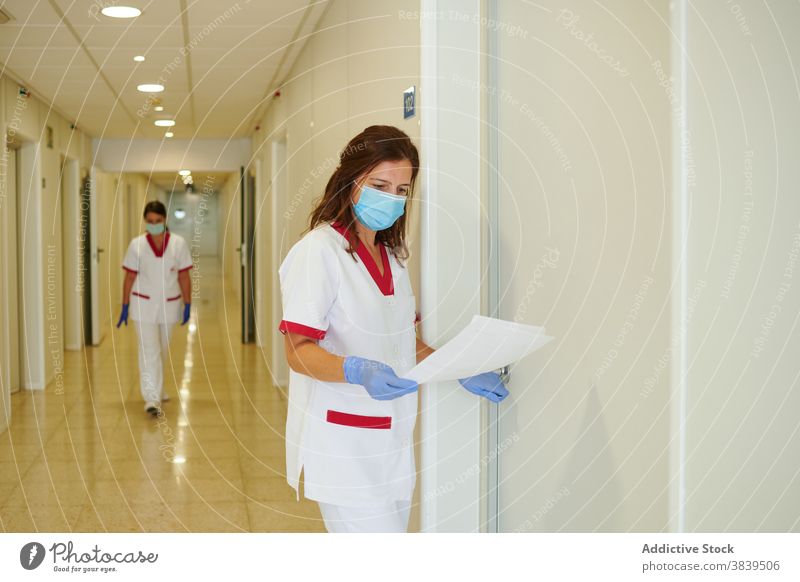 Anonymous nurse in uniform with papers interacting in hospital passage medical staff profession walk women colleague folder colorful corridor professional shiny
