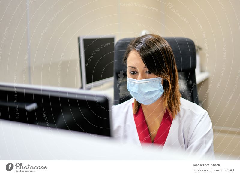 Female clinic administrator working on computer woman staff medical using hospital specialist professional doctor medicine calm robe mask browsing surfing focus