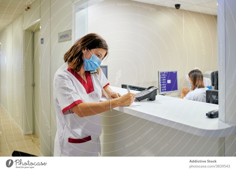 Female doctor signing documents near clinic reception woman take note nurse staff concentrate medicine write work hospital specialist professional calm mask