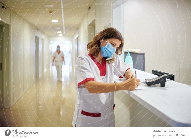 Female doctor signing documents near clinic reception woman take note nurse staff concentrate medicine write work hospital specialist professional calm mask