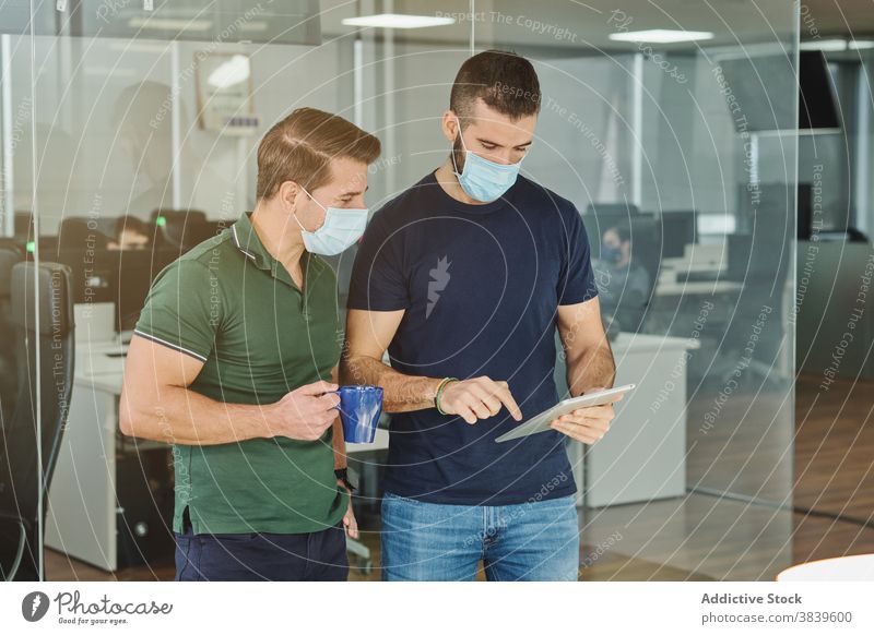 Male coworkers using tablet in office programmer together discuss project programming software developer development coronavirus outbreak job talk employee