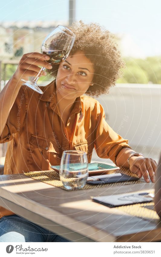 Black woman with wineglass in restaurant examine drink alcohol table cafe female african american black ethnic beverage relax sit happy enjoy smile lady cozy