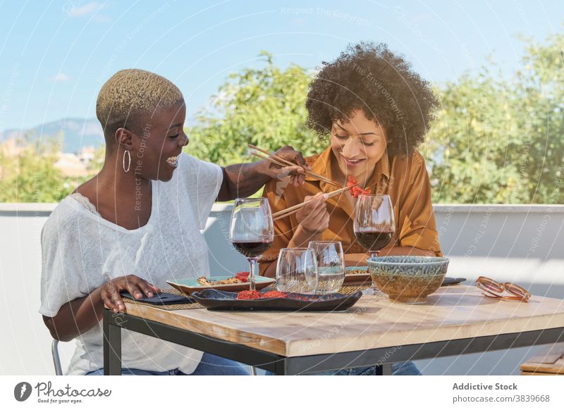 Playful ethnic women having fun at table in restaurant chopstick laugh childish play cheerful friendship food black african american eat terrace together lunch