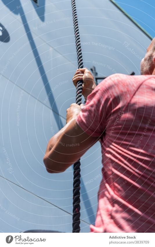Enduring man climbing rope during workout exercise sportsman practice endurance effort strong male athlete healthy confident activity determine summer sunny