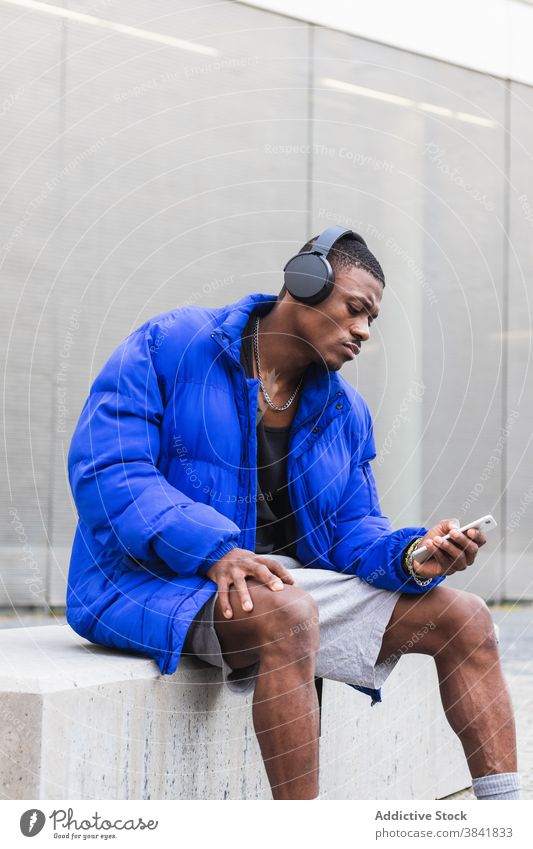 Black man with headphones on smartphone in city listen music calm song wireless street male ethnic black african american jacket young audio peaceful hobby