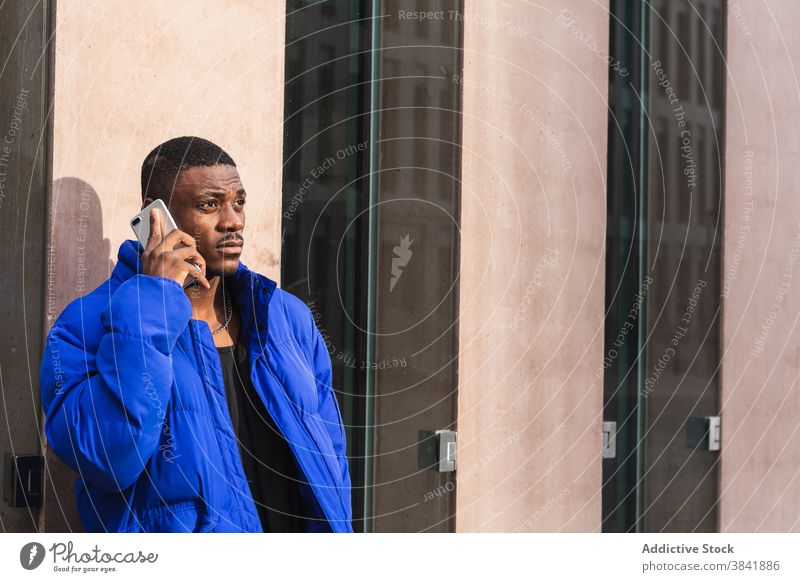 Serious ethnic man talking on smartphone in city phone call speak conversation style urban male black african american warm jacket connection communicate trendy