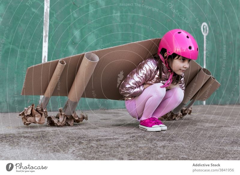 Cute girl in handmade carton wings and helmet in street cardboard child jetpack play kid cute little plane protect sit safety childhood adorable innocent