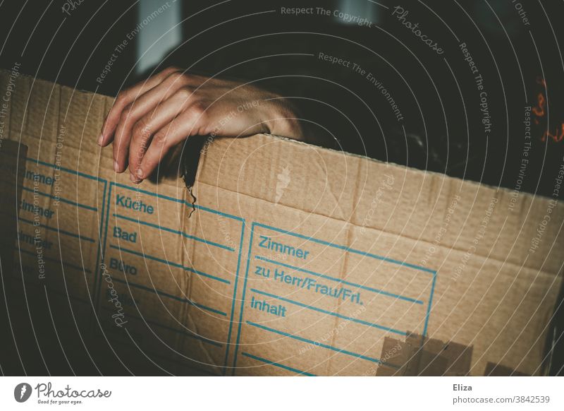 Hand peering out from behind a moving box Packing case relocation Grasp move out Hide Extract change of flat Cardboard Dark Distress Housing search