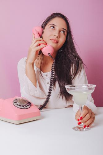 Cheerful and smiling young brunette woman with drink, uses a vintage phone. Portrait on a pink background beautiful brazilian disposable elegance fashion girl