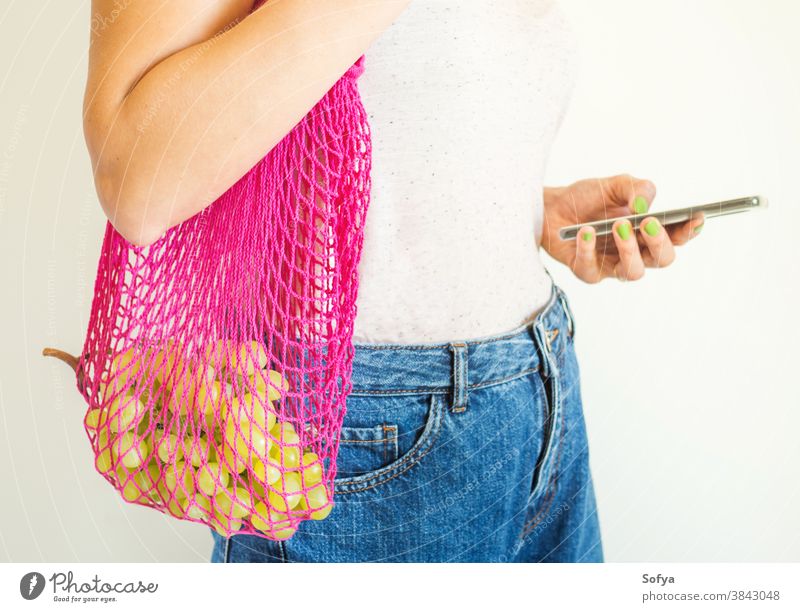 Young woman with reusable mesh bag and smartphone food using mobile phone online delivery grocery fruit grapes autumn plastic sustainable digital zero waste