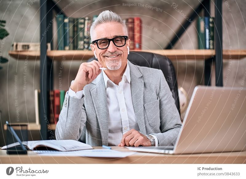 Stylish mature businessman looking at camera and smiling while working in office handsome indoors wireless laptop happy glasses Caucasian entrepreneur computer