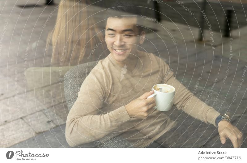 Happy ethnic man drinking coffee in cafe relax weekend coffee shop armchair cozy beverage male asian hot modern cafeteria refreshment comfort mug cup guy young