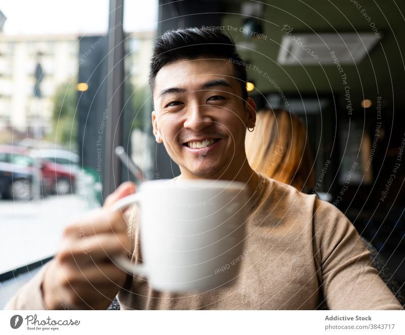 Happy ethnic man drinking coffee in cafe relax weekend coffee shop armchair cozy beverage male asian hot modern cafeteria refreshment calm comfort mug cup guy