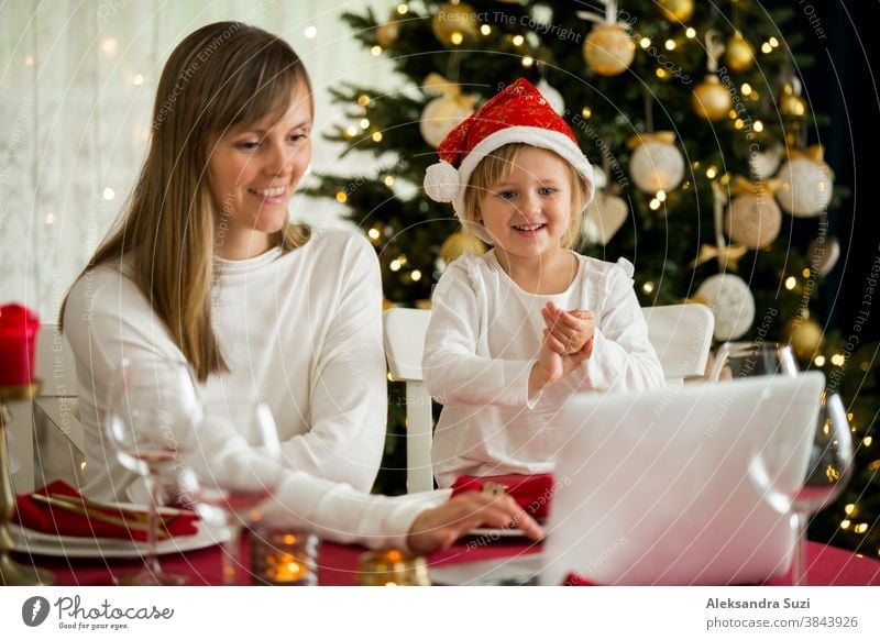 A happy family with a child is celebrating Christmas with their friends on video call using webcam. Family greeting their relatives on Christmas eve online. New normal  virtual event