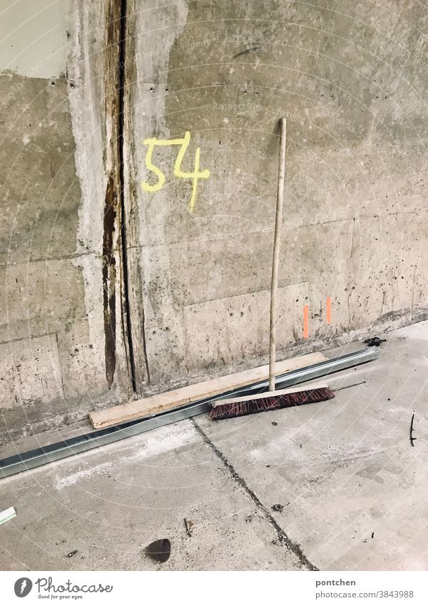 A broom is leaning against a concrete wall.  Construction site. The number 54 is on a wall. Marking Broom Concrete Wall (building) Cleaning Dirty Deserted
