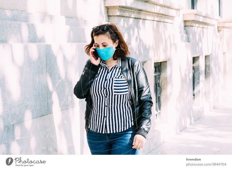 woman with a face mask talks on the phone while walking down the street coronavirus safety person talking adult communication outdoors mobile phone smart phone