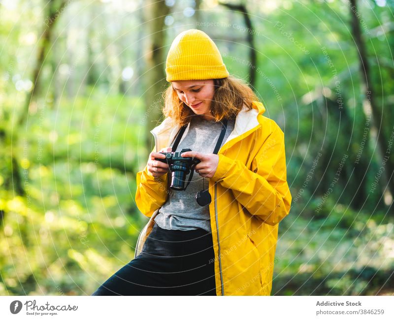Cheerful woman with photo camera in woods photographer traveler yellow raincoat vacation explore stand enjoy cheerful female forest tourist holiday journey