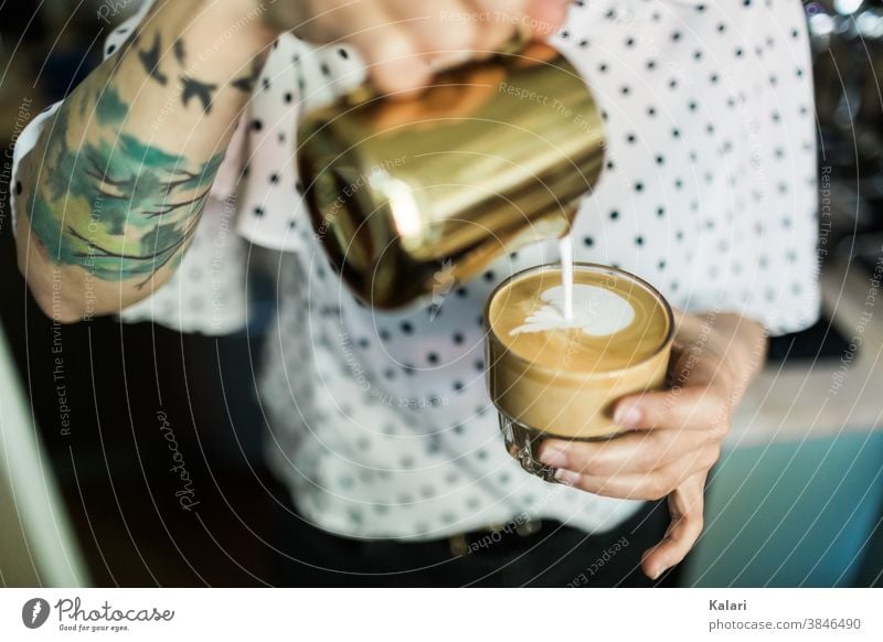 Tattooed barista pours heart into glass of latte with latte art in hand with milk foam Café au lait Cast latte type café au lait Espresso Latte macchiato Coffee