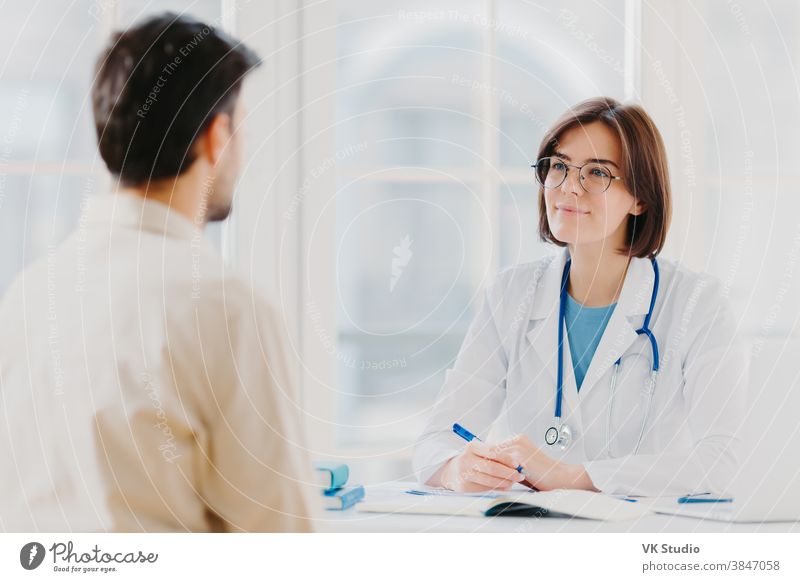 Heathcare, therapy session and assistance concept. Professional woman doctor speaks with male patient, gives consultancy and makes prescription, finds out symptoms of disease, provides help.