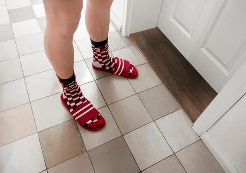 Pale legs stand before a closed door. Checked socks in striped flip-flops. Colour photo Interior shot Legs Boy (child) young man Stand Day Room Hallway