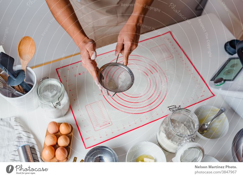 Hands of a man sifting flour by sieve in the table. Eggs bakery desserts butter salt food cooking home home made healthy copy space containers business
