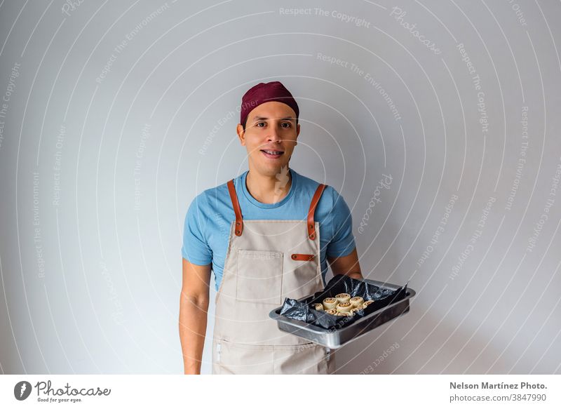 Hispanic man holding a tray of cinnamon rolls in a white background. adult indoor cooking dough flour chef restaurant employment food Eggs bakery desserts
