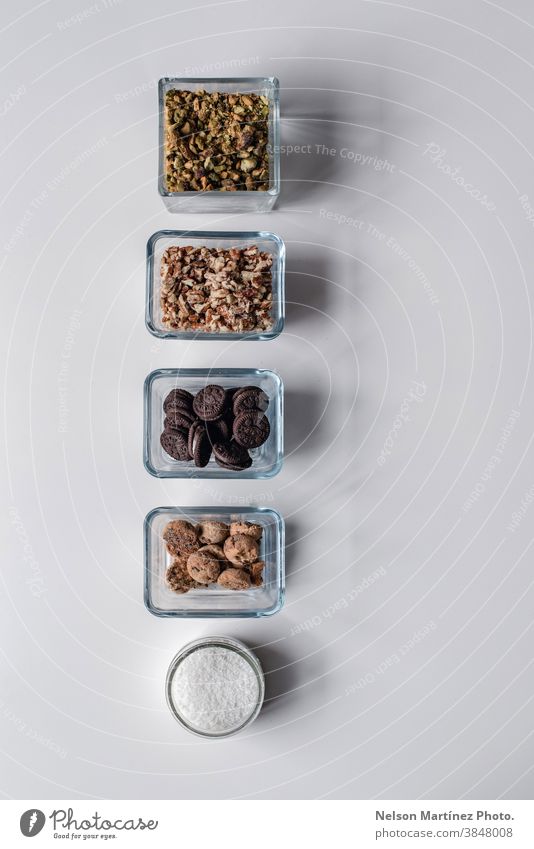 Row of ingredients in small containers with pistachio, nuts, cookies, and desiccated coconut. cooking chef kitchen raw white table composition elements sweet