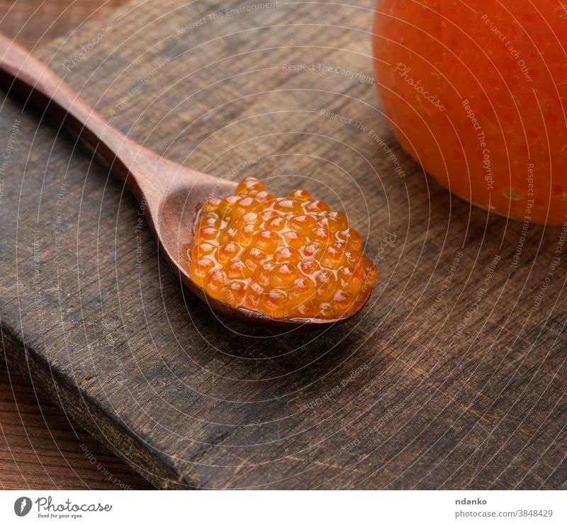 red caviar in a wooden brown spoon on the table, behind a full jar of caviar food seafood fish luxury pink salmon gourmet closeup orange tasty salty
