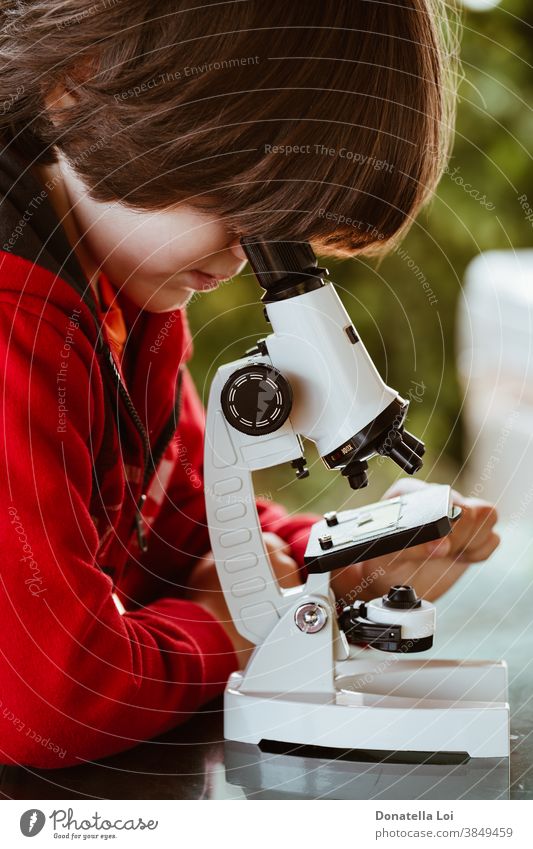 Child looking through a microscope attention casual clothing caucasian child childhood concept curiosity curious explore kid learning lifestyle male nature new