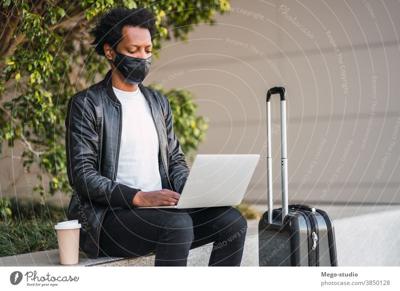 Afro tourist man using his laptop outdoors. afro travel protective mask portrait casual connection holiday tourism virus disease covid-19 notebook network urban