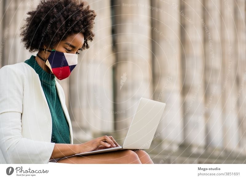 Business woman using her laptop outdoors. young afro business urban street success device face mask information protect protective mask covid-19 connection