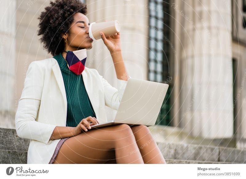 Business woman using her laptop outdoors young afro business urban street success device corporate information coffee face mask protective mask connection