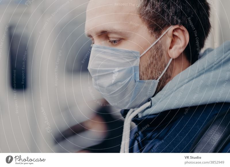 Close up shot of serious man walks in crowded places, commutes to work in underground, wears medical mask for face protection during outbreak and coronavirus infection. Disease protection concept