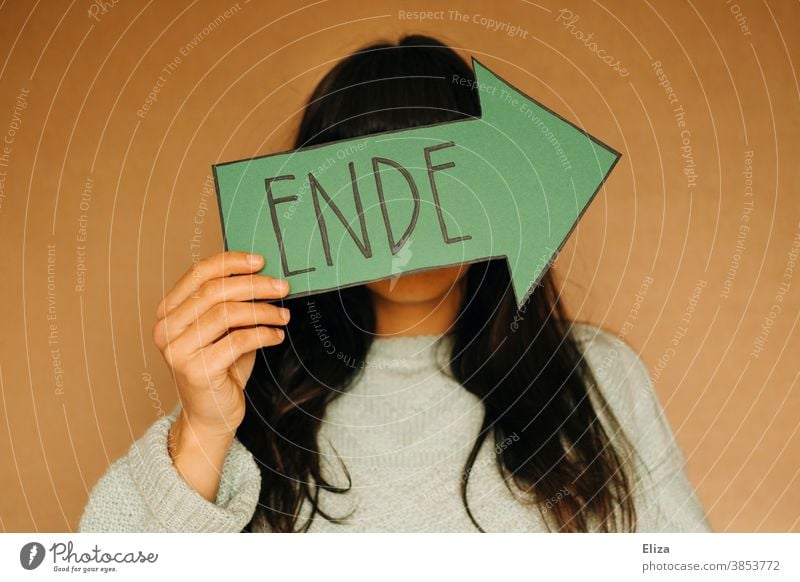 Woman holding a green arrow with the word end written on it. Separation, off, over. End Divide from Transience Green Past Hand sign Arrow Direction Orientation