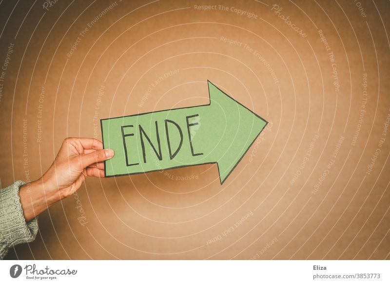 Hand holds a green arrow with the word end written on it. Separation, off, over. End Divide from Transience Green Past sign Arrow Direction Orientation