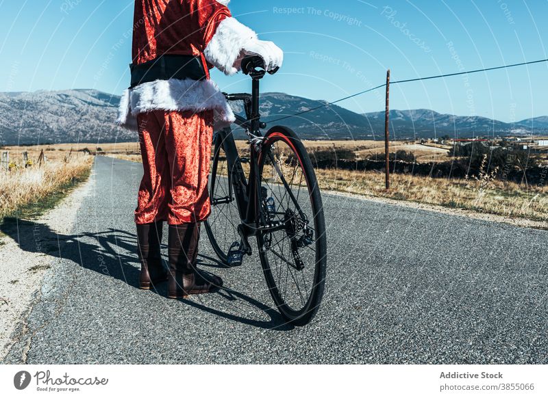 Anonymous Santa Claus near bicycle on road in countryside santa claus relax roadway vehicle bike santa hat male beard costume red color modern style stand