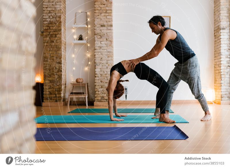 Man and woman doing yoga together help lesson instructor wheel pose bend support studio practice young adult wellness asana class balance zen wellbeing stretch