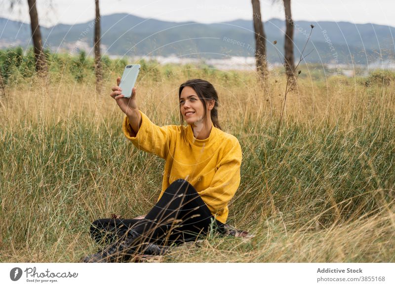 Smiling woman taking selfie in meadow in fall autumn relax smartphone self portrait charming weekend enjoy female sweater yellow dry field device gadget nature