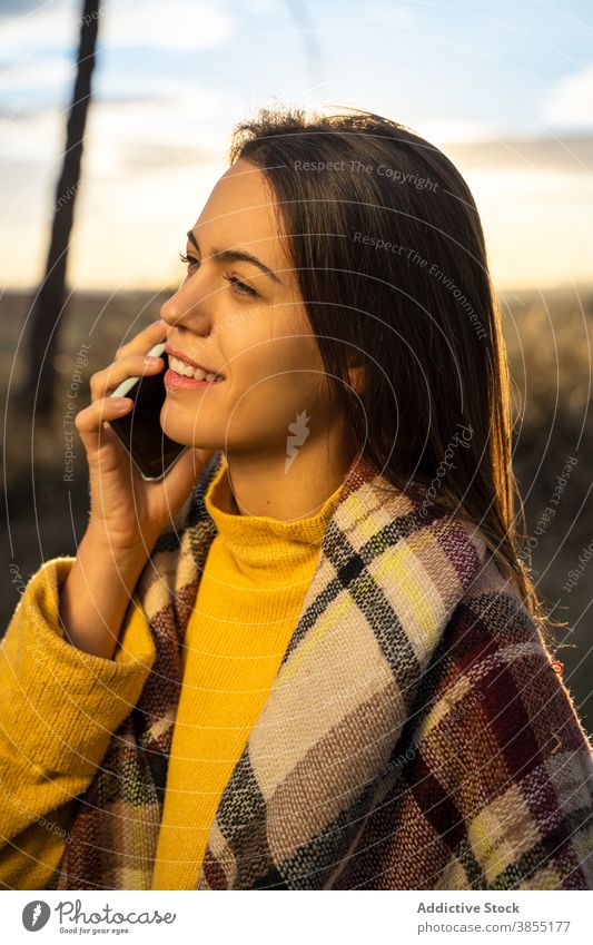 Delighted woman talking on smartphone at sunset autumn park speak relax enjoy weekend female cellphone sundown smile conversation cheerful happy chat fall