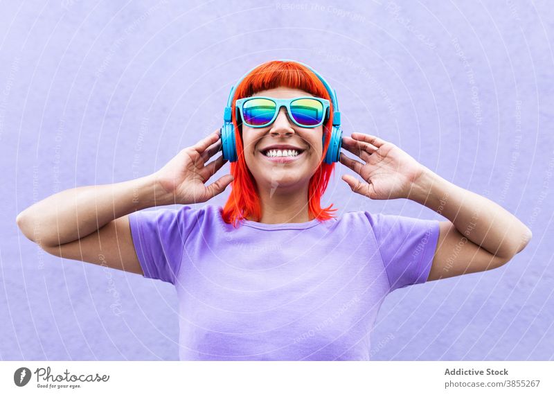 Excited redhead woman listening to music sign happy street city rebel colorful bright female adult millennial loud scream headphones touch ginger dyed hair wall