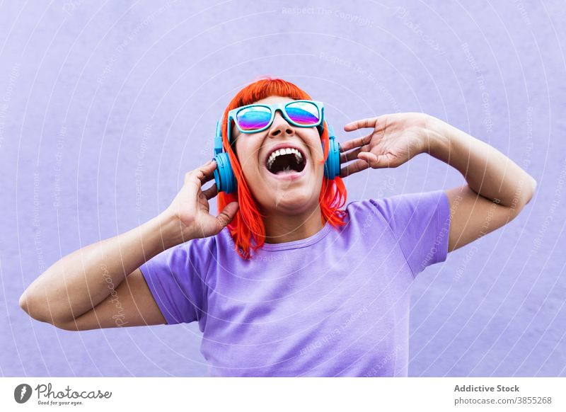 Excited redhead woman listening to music sign happy street city rebel colorful bright female adult millennial loud scream headphones touch ginger dyed hair wall