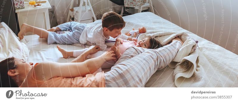 Relaxed mother and sons playing over the bed covid-19 confinement family child panoramic panorama laugh cheerful smiling smile happiness coronavirus