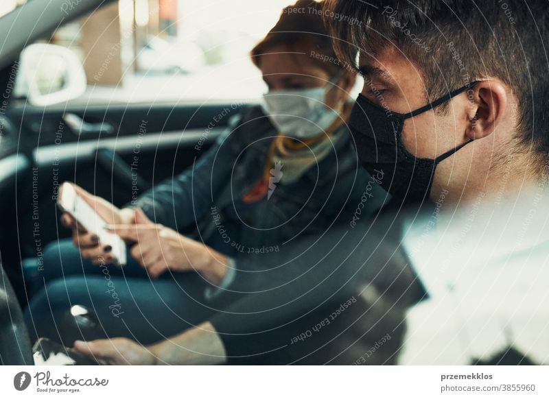 Man and woman sitting in a car using smartphones wearing the face masks to avoid virus infection caucasian covid-19 lifestyle outbreak outdoors pandemic