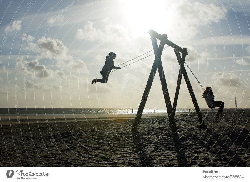 Two girls are swinging towards the sky on the beach of Norderney. Human being Child Girl Infancy Environment Nature Landscape Sun coast Beach North Sea Happy